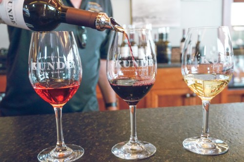 A person pours red wine into a glass, alongside two other glasses of white and rosé wine at Kunde Family Winery.
