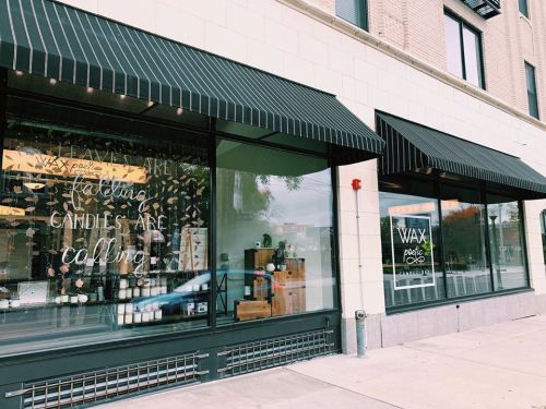 Storefront with large windows displaying candles and decorative text: "Wax poetic, candles are calling." Black awnings above.