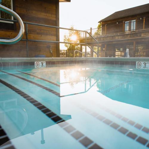 A serene swimming pool at sunset, with steam rising and a wooden building in the background.