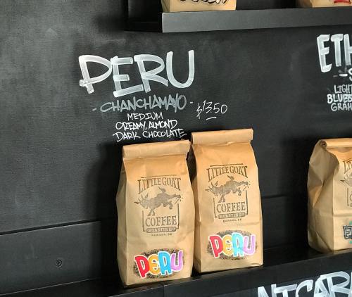Brown paper coffee bags labeled "Peru" and "Chanchamayo" on a black wall, with prices and tasting notes.
