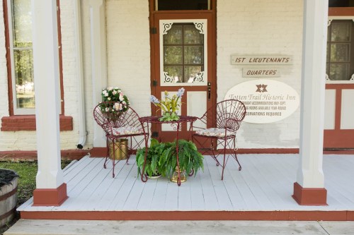 A cozy porch with two red chairs, a small table, and potted plants, inviting relaxation at a historic inn.