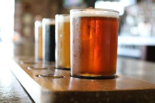 A wooden flight board with four glasses of different beers, showcasing a variety of colors and styles.