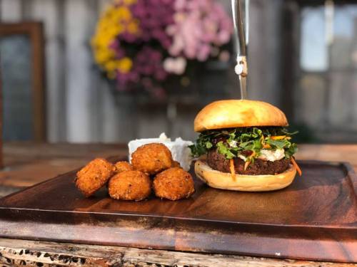 A gourmet burger topped with fresh greens on a wooden board, accompanied by crispy golden croquettes.