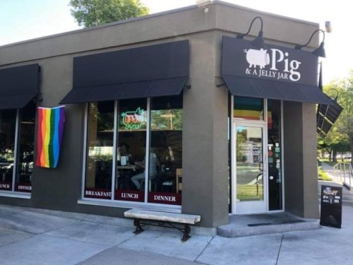 Exterior of Pig & A Jelly Jar restaurant with a rainbow flag, featuring awnings and a bench outside.