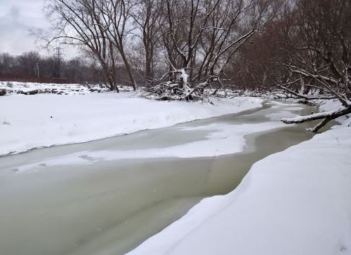 A snowy landscape featuring a frozen river surrounded by bare trees and a white blanket of snow.