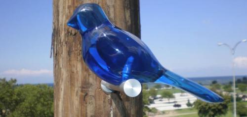 A blue glass bird sculpture perched on a wooden post against a clear sky and distant landscape.