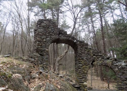 Stone ruins with arched openings, surrounded by trees in a forested area.