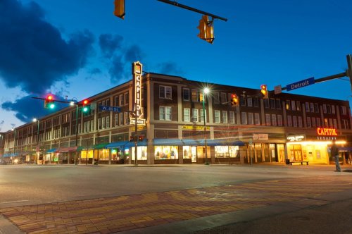 A street view at dusk featuring a historic building with neon signs and traffic lights in a city setting.
