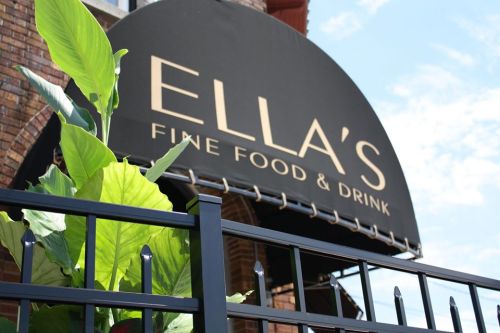 Sign for Ella's Fine Food & Drink, featuring a black awning and green plants in front, against a blue sky.