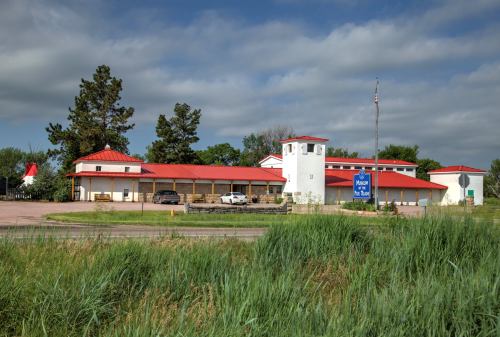 A white building with a red roof and tower, surrounded by greenery, along a highway with a sign for a motel.
