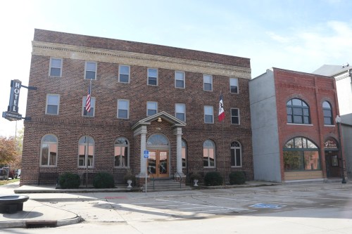 Historic brick hotel building with columns, flags, and large windows, located on a city street.