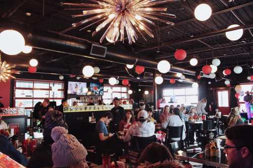 A lively restaurant interior with colorful decor, hanging lights, and patrons enjoying their meals at tables.