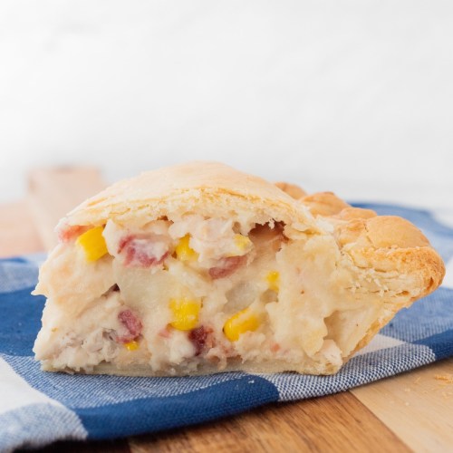 A slice of savory pie filled with creamy potato, corn, and meat, resting on a blue checkered cloth.