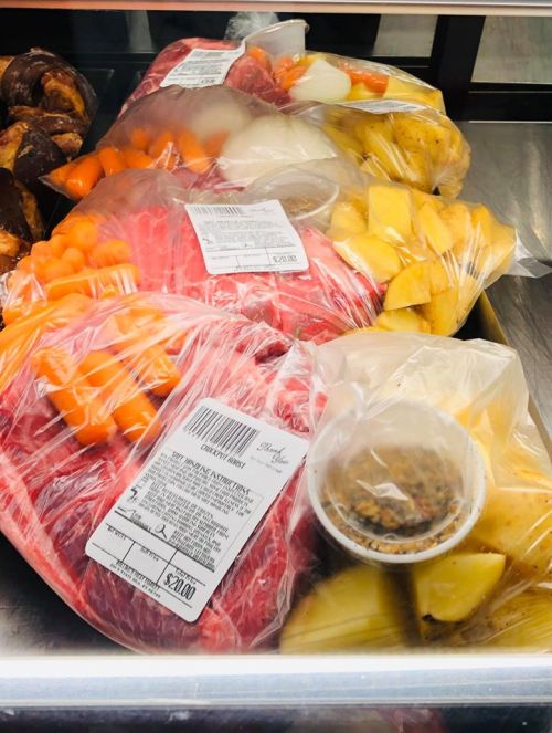 Packages of meat, vegetables, and a container of sauce, all wrapped in plastic, displayed on a tray.