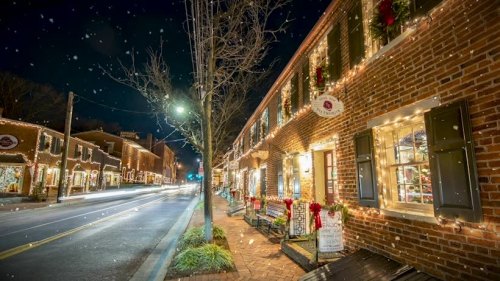 A charming street lined with brick buildings adorned with festive lights and decorations, set against a night sky.