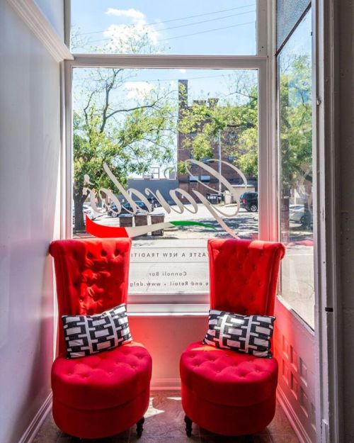 Two red tufted chairs with patterned pillows sit by a large window, letting in bright natural light.