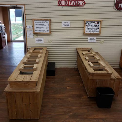 Two wooden tables with open slots, set up for gem mining, inside a building with a sign for Ohio Caverns.