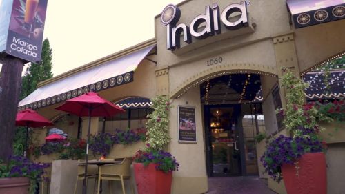 Exterior of a restaurant named "India," featuring red umbrellas and vibrant flower pots.