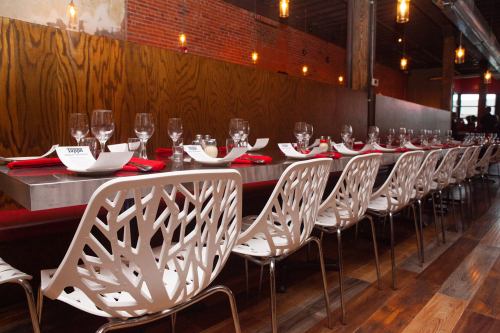 A long dining table set with glasses and red napkins, surrounded by modern white chairs in a stylish restaurant.
