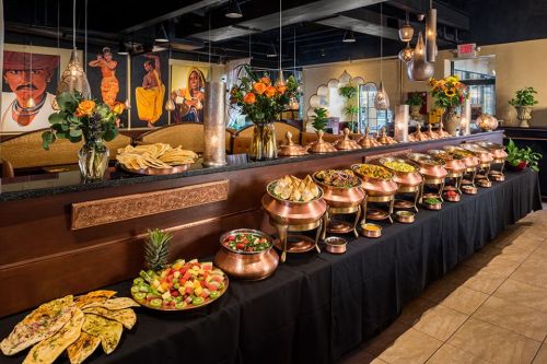 A buffet table filled with various dishes, including salads, breads, and colorful vegetables, set in a vibrant restaurant.