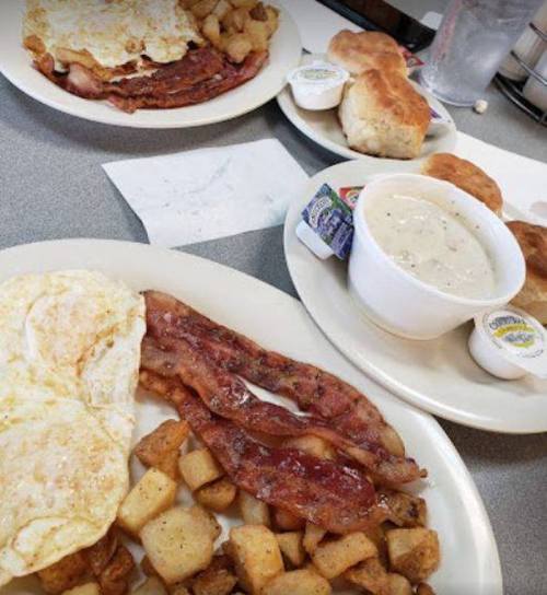 A hearty breakfast spread featuring eggs, bacon, hash browns, biscuits, and gravy on a table.