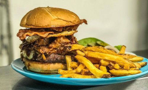 A hearty burger topped with bacon and crispy onions, served with a side of golden French fries on a blue plate.