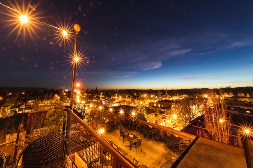 A rooftop view of a city at dusk, illuminated by warm lights and a deep blue sky.