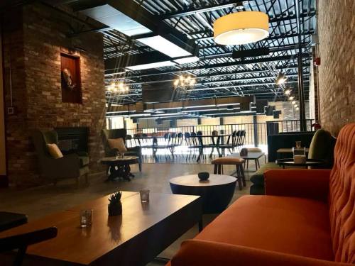A modern, spacious lounge with brick walls, stylish furniture, and a large dining table under industrial lighting.