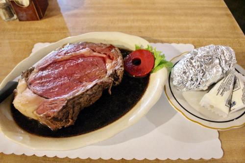 A large serving of prime rib on a plate, accompanied by a baked potato wrapped in foil and a slice of lettuce.