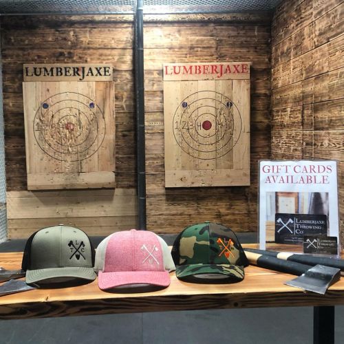 Three hats in front of two axe-throwing targets, with a sign for gift cards available at LumberJaxe.