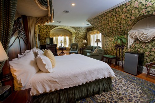 Luxurious bedroom with floral wallpaper, a large bed, seating area, and elegant decor.
