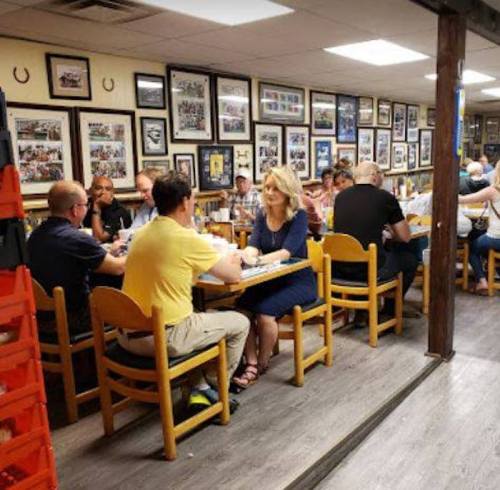 A busy restaurant with patrons seated at wooden tables, surrounded by framed photos on the walls.