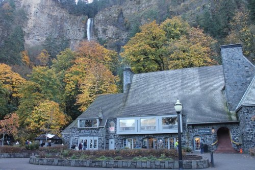 A stone building surrounded by vibrant autumn trees, with a waterfall cascading in the background.