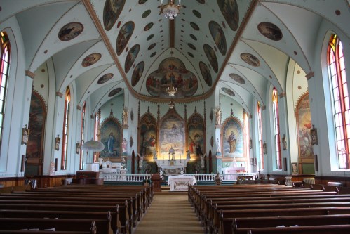 Interior of a beautifully decorated church with colorful murals, stained glass windows, and wooden pews.