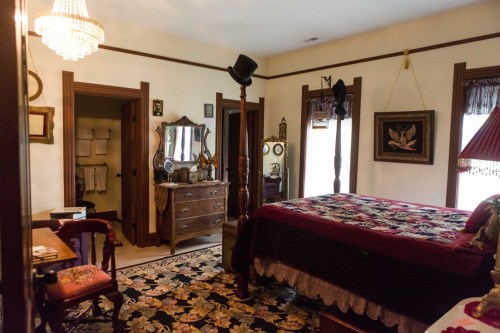 A vintage bedroom with a four-poster bed, ornate decor, a chandelier, and a patterned rug.
