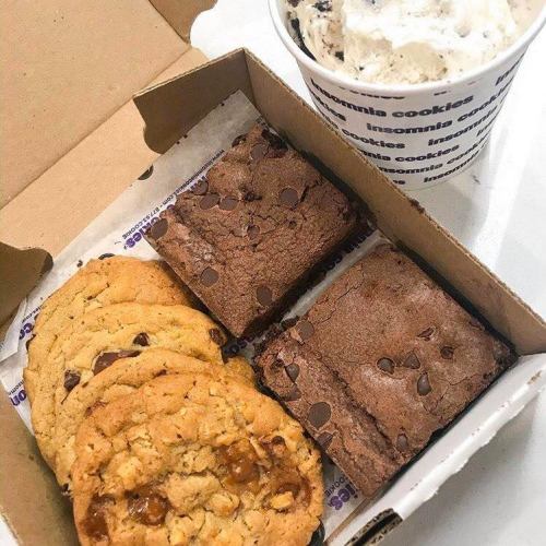 A box of assorted cookies and brownies alongside a cup of cookie dough ice cream.