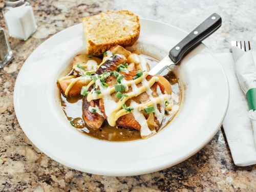 A plate of grilled chicken with sauce, topped with green onions, served with a slice of bread on the side.