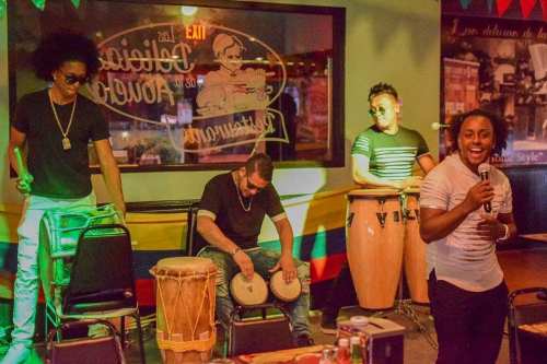 A lively music performance with two musicians on congas and a singer, set in a colorful venue.