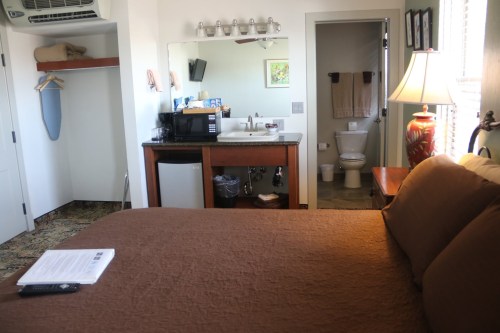 Cozy hotel room with a brown bedspread, kitchenette, and bathroom visible in the background.