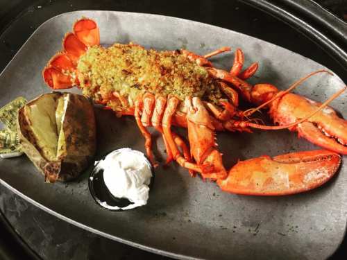 A baked lobster topped with stuffing, served with a baked potato and sour cream on a gray plate.