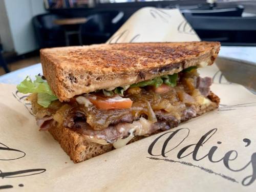 A toasted sandwich filled with roast beef, melted cheese, lettuce, tomatoes, and caramelized onions on brown bread.