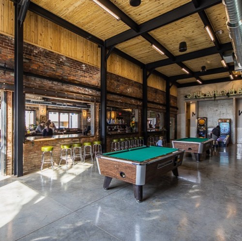 A spacious bar area with pool tables, wooden beams, and a modern industrial design.