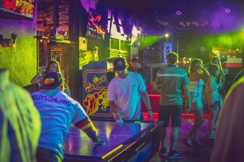 A lively bar scene with people playing games, colorful lights, and a vibrant atmosphere.