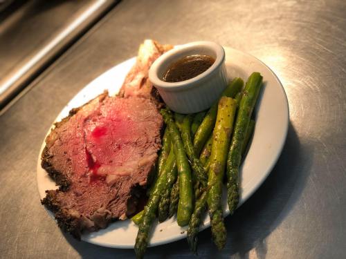 A plate with sliced roast beef, asparagus, and a small bowl of sauce on a metallic surface.