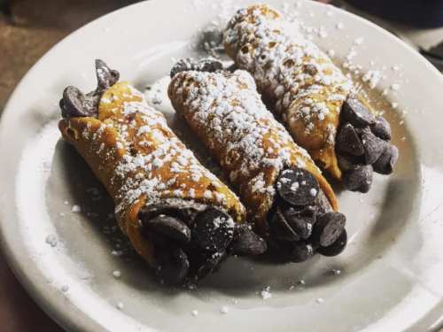 Three cannoli filled with chocolate chips, dusted with powdered sugar, served on a white plate.