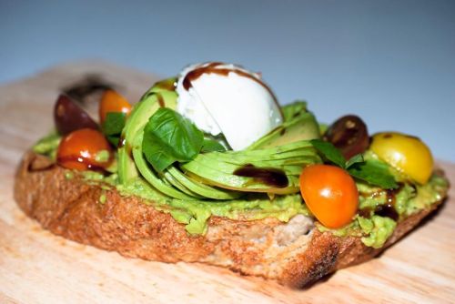 Avocado toast topped with cherry tomatoes, fresh basil, and a scoop of creamy burrata on rustic bread.
