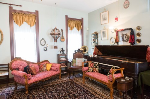 A vintage living room with ornate furniture, a piano, and decorative wall art, featuring warm colors and a cozy atmosphere.