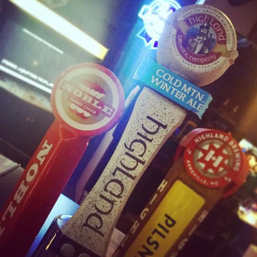 Close-up of beer taps featuring Noble Hard Cider, Highland Brewing, and Cold Mountain Winter Ale at a bar.