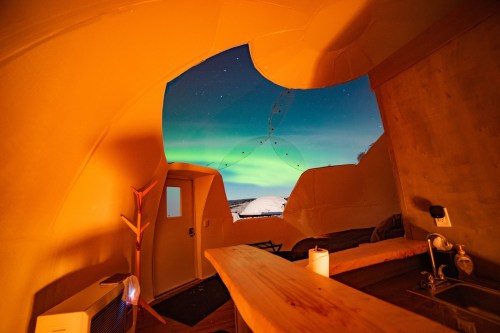 Interior of a cozy dome with a view of the night sky and northern lights through a large, circular window.