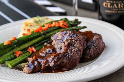 A plate of steak with sauce, asparagus, and mashed potatoes topped with diced tomatoes.